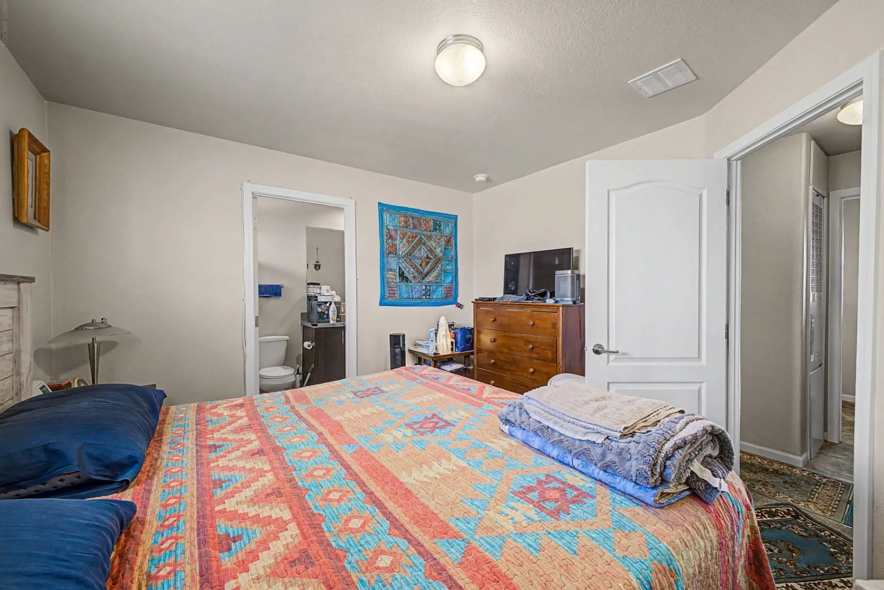 Additional bedroom view with a patterned quilt, dresser, and adjoining bathroom doorway